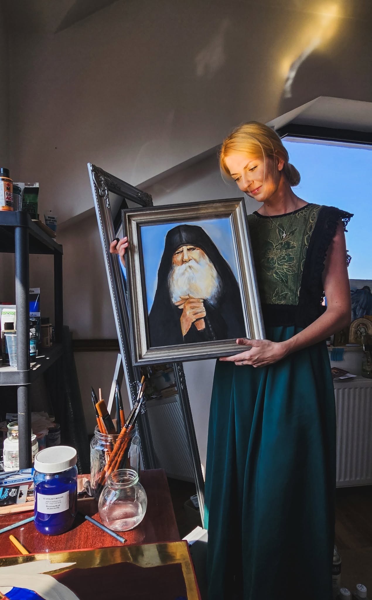 Anita M. Frâncu ținând un portret înrămat al unui părinte, în atelier.
