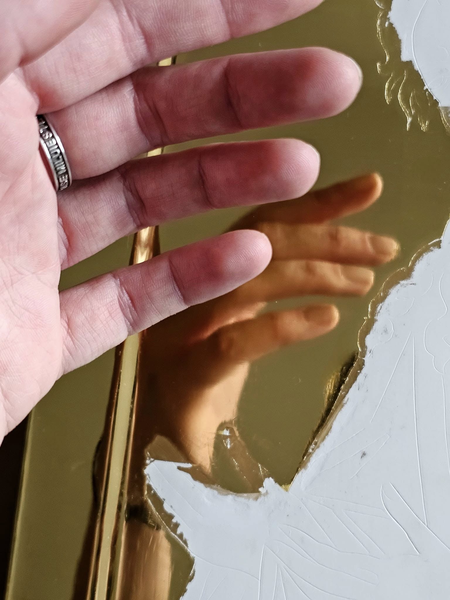 Reflexia unei mâini în suprafața aurie a panoului, lângă desenul incizat.