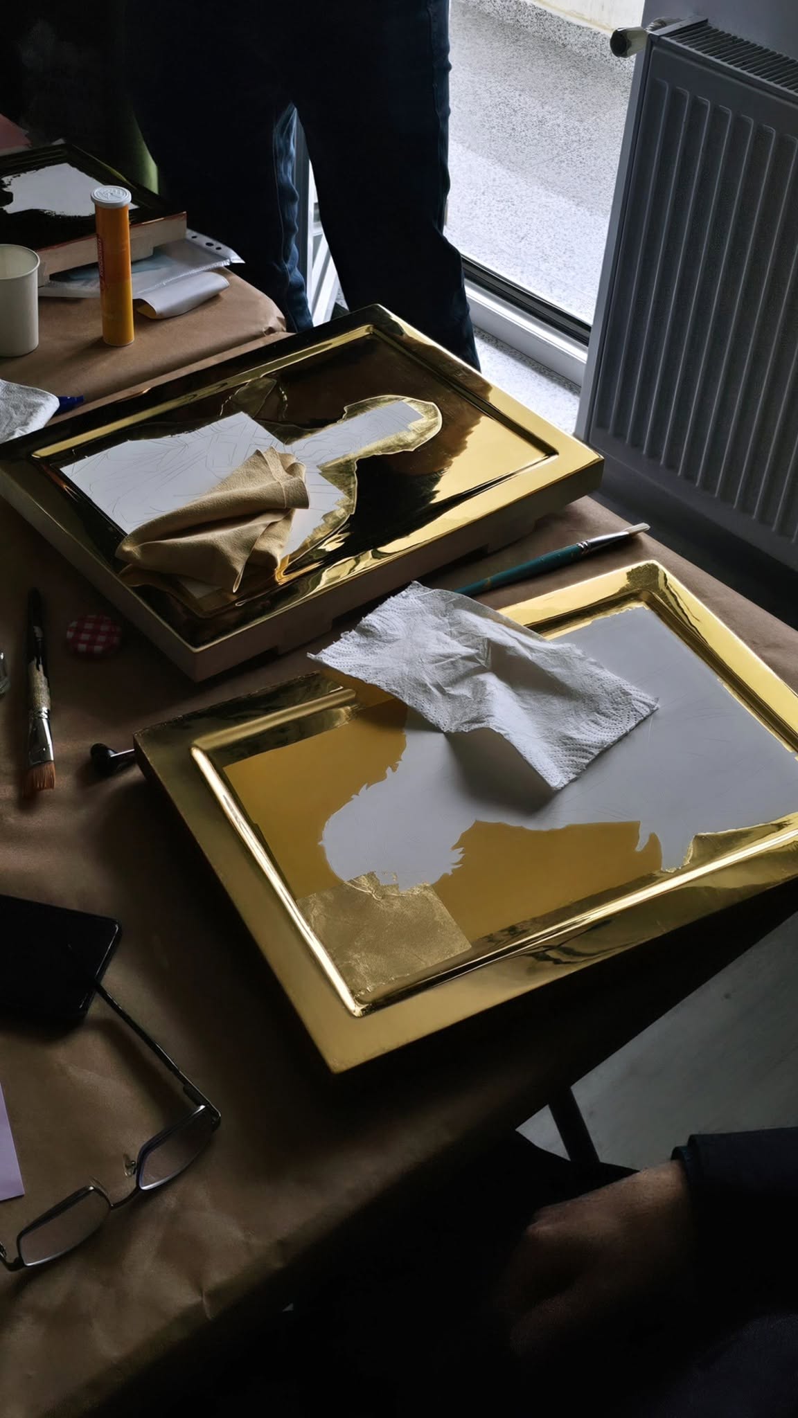 Două panouri cu fundal auriu și desene pregătitoare, pe masa de lucru.