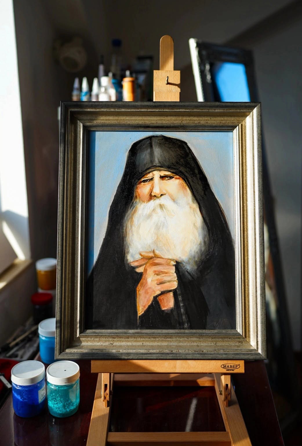 Portret pictat al unui părinte cu barbă albă și veșmânt negru, pe fundal albastru.