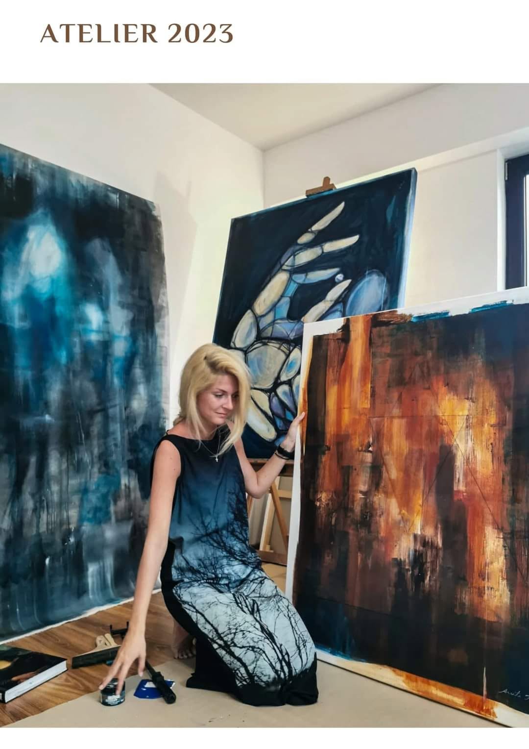 Artista în atelier, alături de compoziții în albastru, alb și ocru.