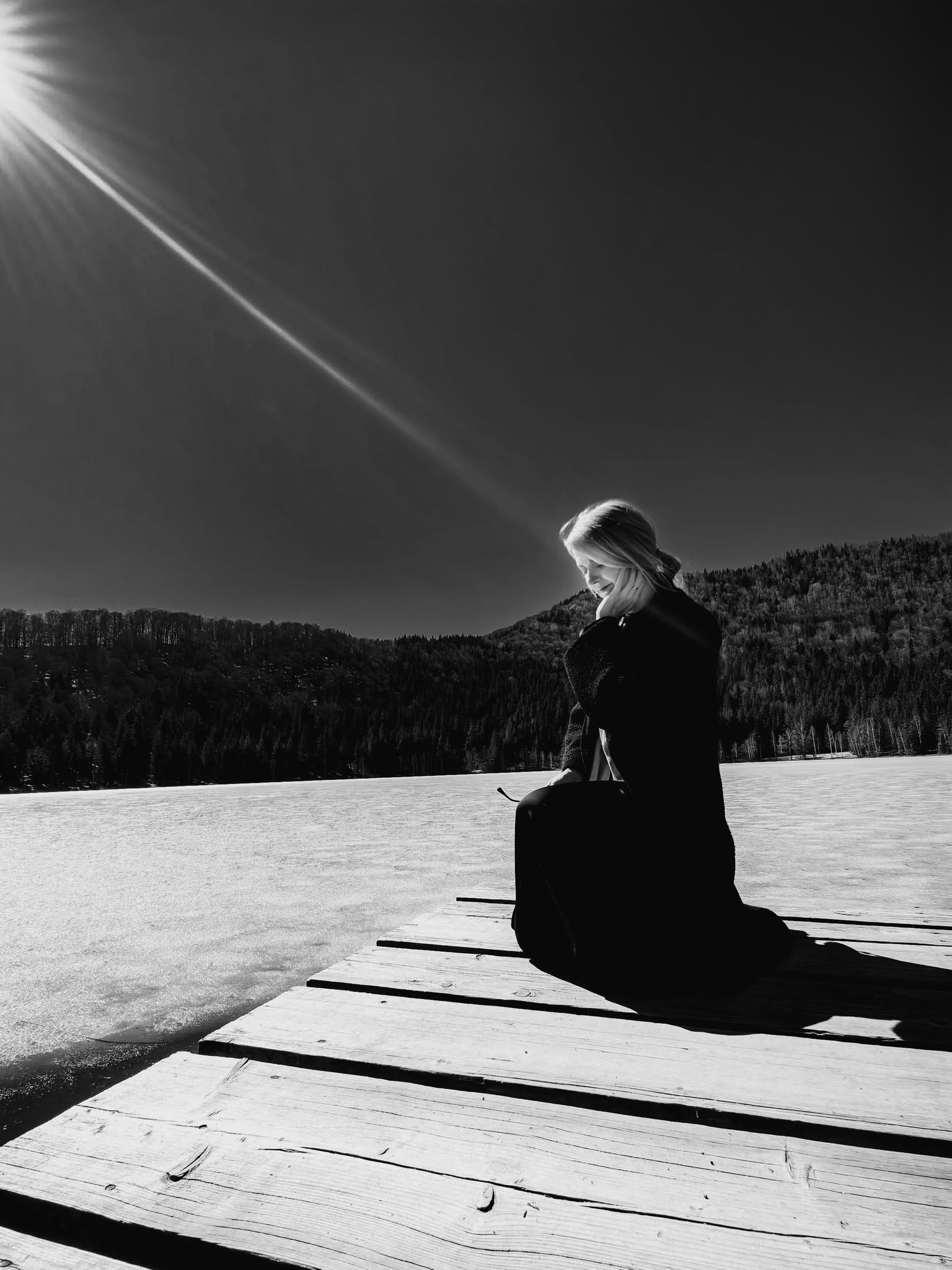 Fotografie alb-negru cu artista așezată lângă un lac, într-un peisaj de iarnă.
