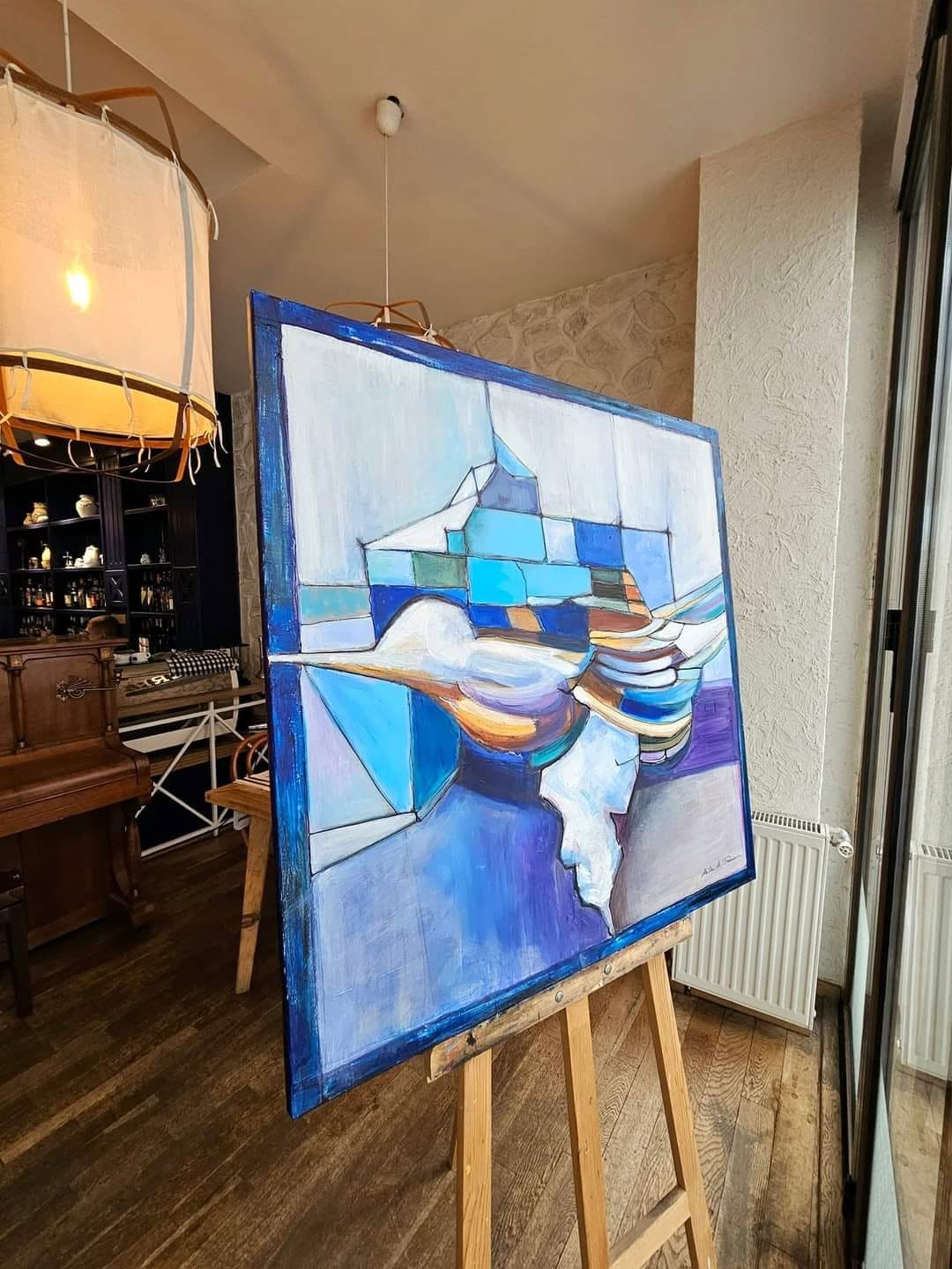 Lucrarea Zborul / Pasărea Măiastră, prezentată pe un șevalet lângă fereastră.
