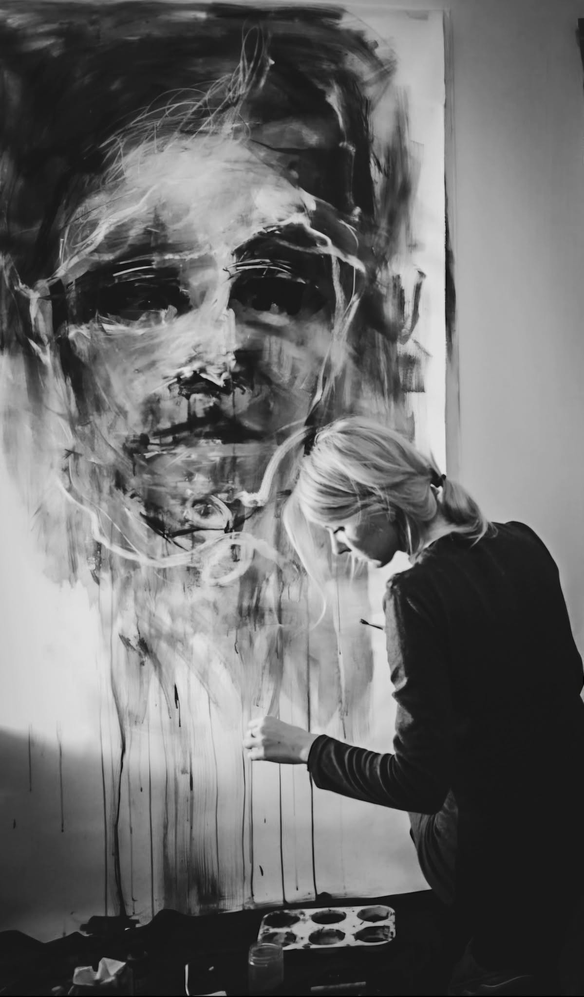 Anita M. Frâncu pictând în atelier, în fața unui portret de mari dimensiuni.