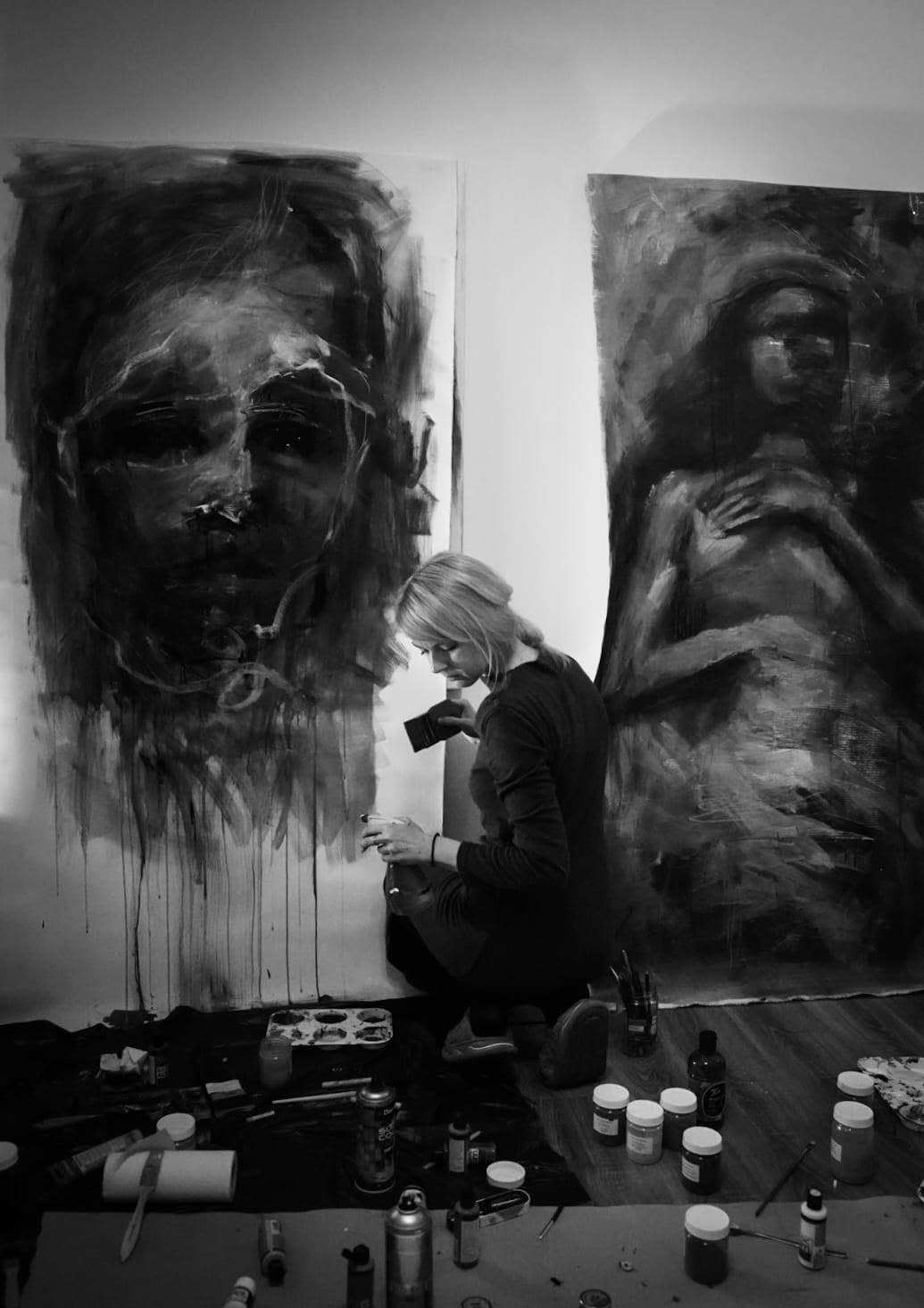 Artista lucrând la baza unui portret, înconjurată de materiale de pictură.