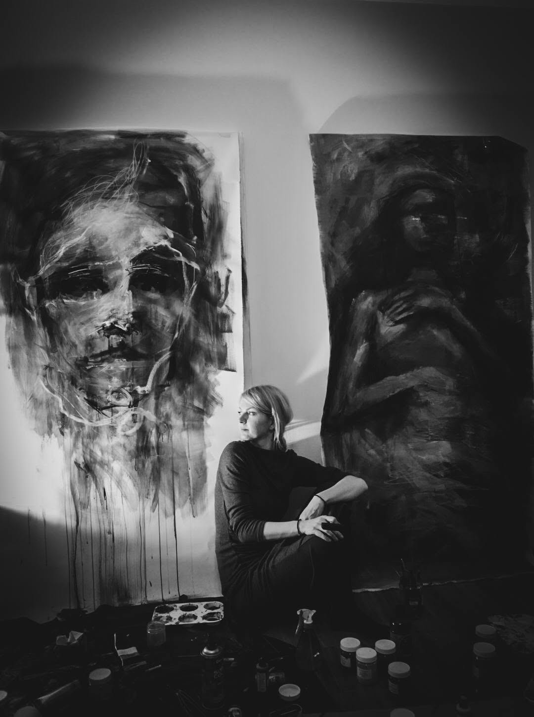 Artista așezată între două compoziții figurative, în atelier.