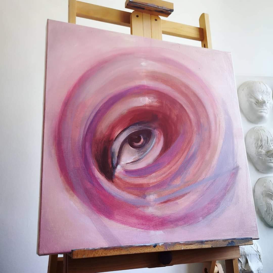 Un ochi în centrul unor forme circulare în roz și violet, pe șevalet.