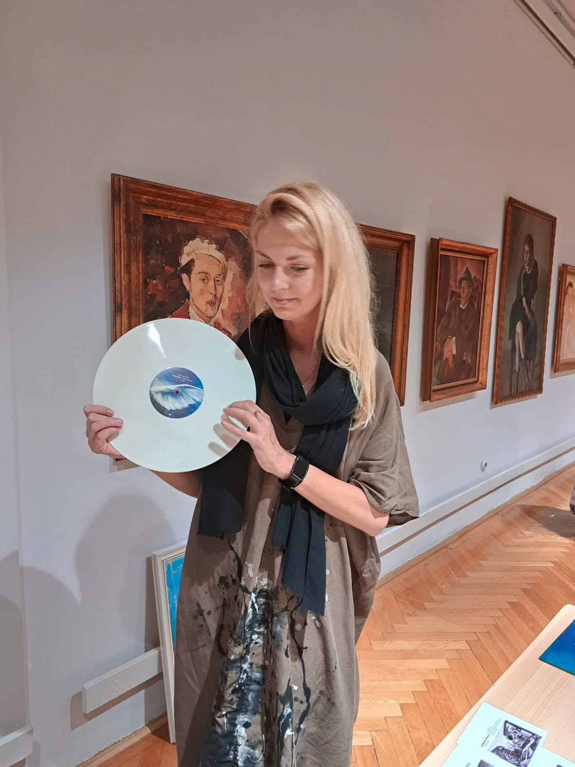 Anita Frâncu ținând un disc de vinil deschis la culoare, în galeria muzeului.